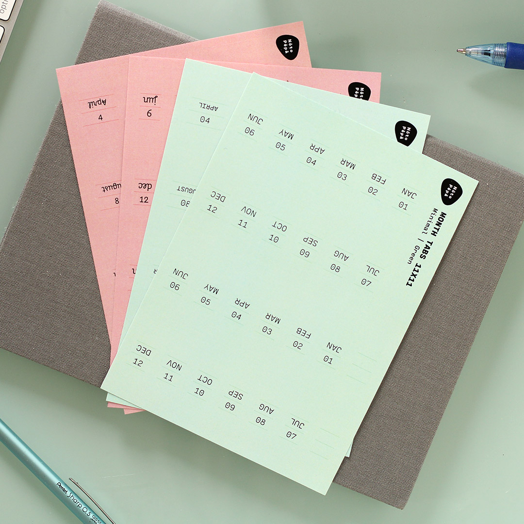 Noto Pepa all Pink & Green Abbreviated Month Tabs Stickersheets for two years on a bullet journal notebook on work desk with keyboard